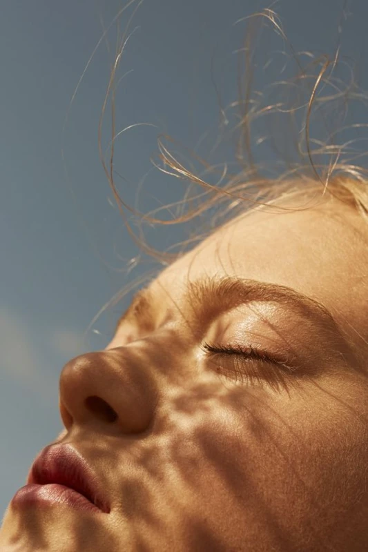 Chica relajada con los ojos cerrados, disfrutando de la serenidad bajo el sol, reflejando la paz interior alcanzada en nuestros eventos de meditación en Barcelona.